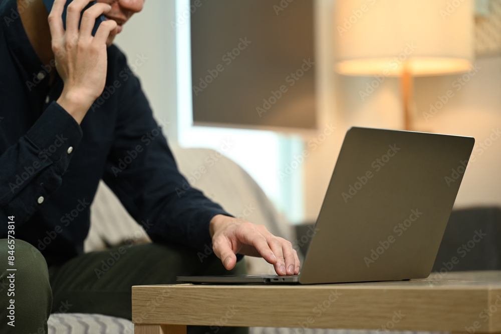 Cropped shot male freelancer talking on mobile phone and using laptop at home Cropped shot male freelancer talking on mobile phone and using laptop at home