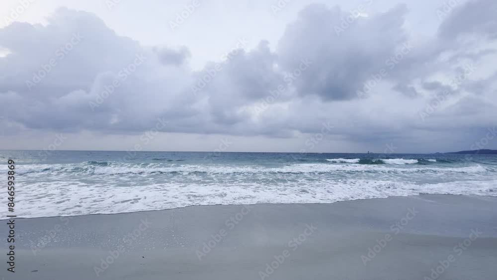 Gray sky and sea with foamy waves crashing against the shore.