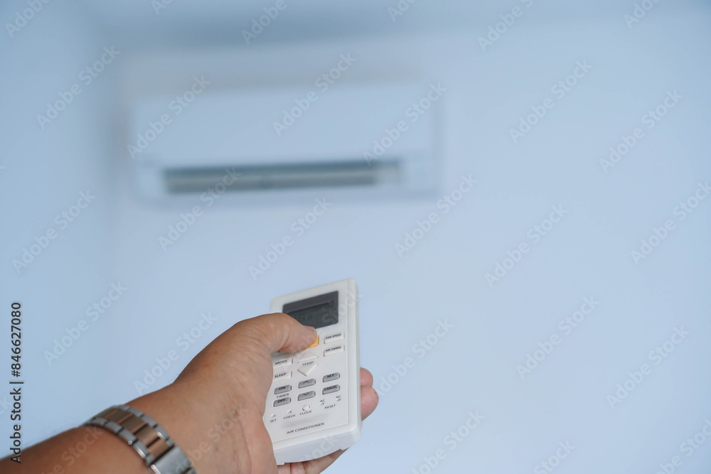 A person is holding a remote control in front of a white air conditioner A person is holding a remote control in front of a white air conditioner