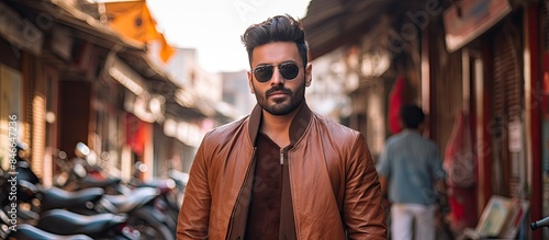 A stylish Indian man is posing in an urban setting, showcasing street fashion and style in front of a copy space image.