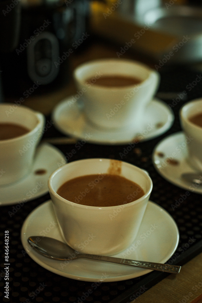 Cocoa bean tea packet in a white glass on a wooden table with chocolate chunks next to it surrounded by seeds.