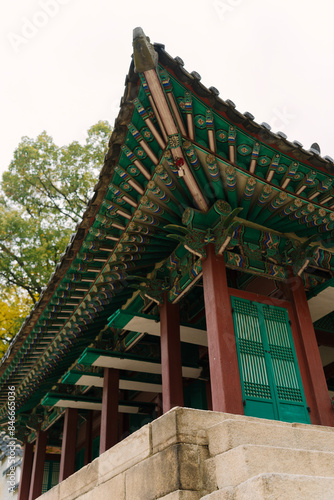 a traditional Korean pavilion with a tiled roof and green window details, set amidst lush trees in Changdeokgung Palace’s Biwon Garden, Seoul. photo