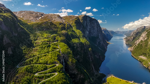 Fotografi An aerial view of a winding road snaking through a lush green valley, culminating at the edge of a stunning fjord in Norway