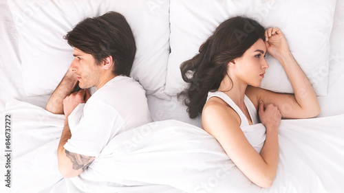 Photos A young couple lies in bed, turned away from each other, seemingly after an argument