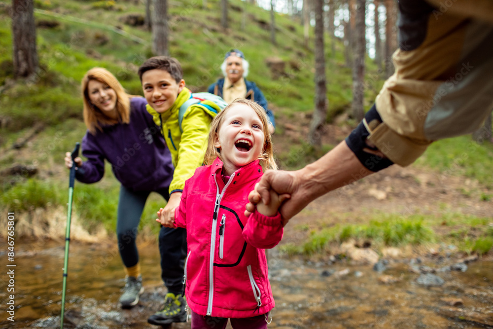 Multi-generational family crossing a stream during a forest hike Multi-generational family crossing a stream during a forest hike