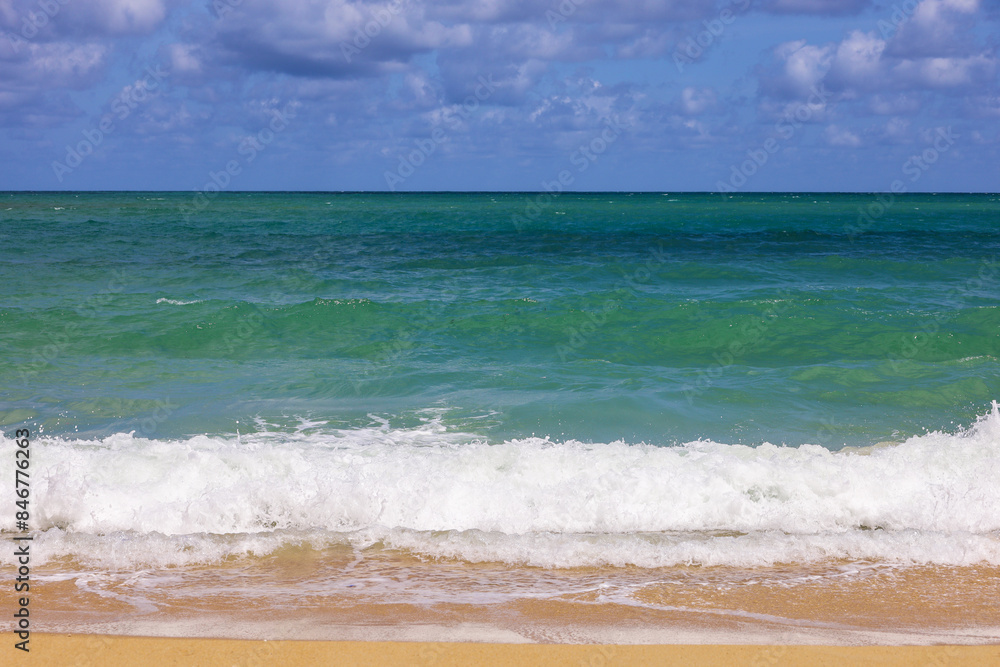 Empty sea beach with yellow sand, view to emerald green waves and blue sky with clouds Empty sea beach with yellow sand, view to emerald green waves and blue sky with clouds