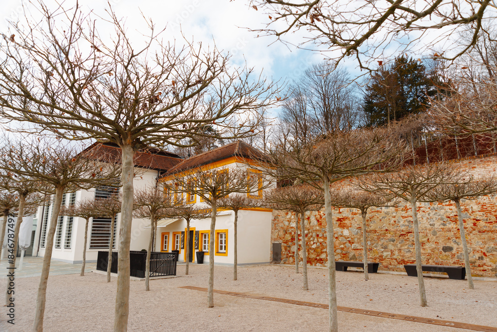 A serene courtyard with leafless trees and an ancient edifice in the backdrop, set against a cloudy sky A serene courtyard with leafless trees and an ancient edifice in the backdrop, set against a cloudy sky