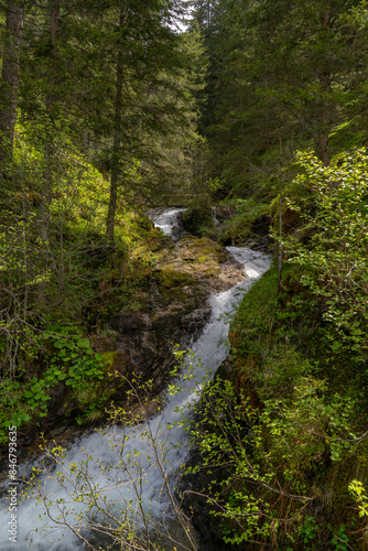 bridge over troubled water, white waterfall and bridge in the high mountains at the edge of the forest. meltwater flows down the mountain. Steep terrain with river, stream in Vorarlberg, Austria