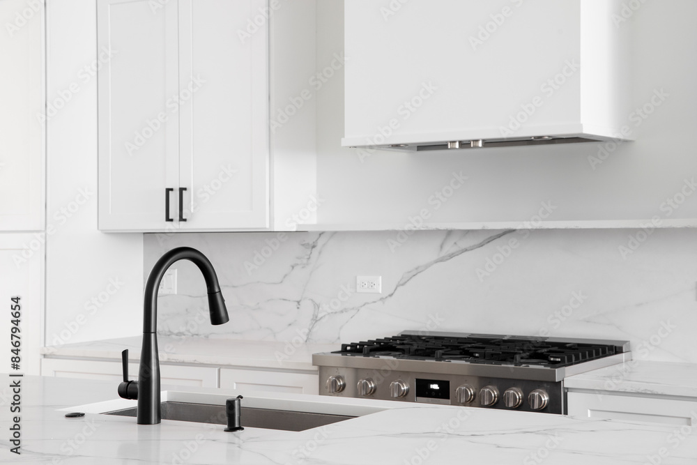 Ταπετσαρία An all white kitchen with a black faucet on a white marble countertop with a stainless steel stove below a white range hood and marble backsplash