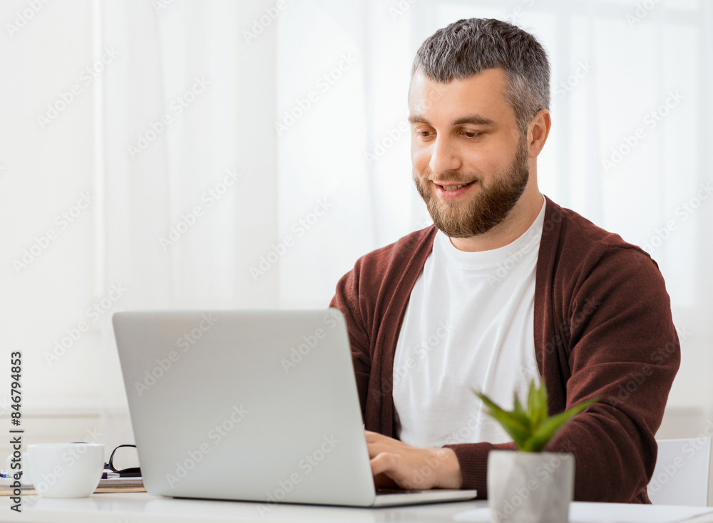 A man is seated in front of a laptop computer, focused on the screen with a serious expression. He is typing on the keyboard and appears to be working or studying intently. A man is seated in front of a laptop computer, focused on the screen with a serious expression. He is typing on the keyboard and appears to be working or studying intently.