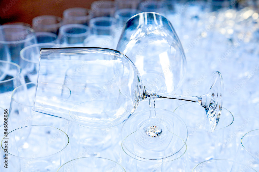 Two red wine crystal glasses lay on a raw of other grasses prepared for big party. Blurred. Catering and restaurant utensils. wedding organisation. Wine tasting. Background picture. Group of objects Two red wine crystal glasses lay on a raw of other grasses prepared for big party. Blurred. Catering and restaurant utensils. wedding organisation. Wine tasting. Background picture. Group of objects