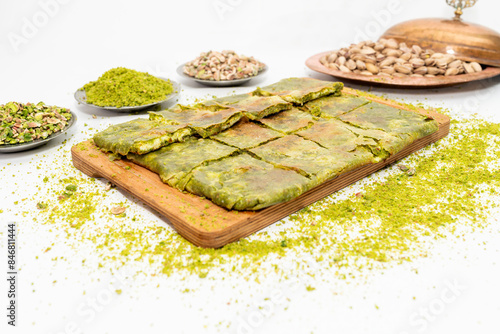 Traditional Turkish dessert Katmer with clotted cream and dough on wooden board isolated on white background. Prepared with thin dough, green ground pistachio and sherbet. Dessert of Gaziantep region.