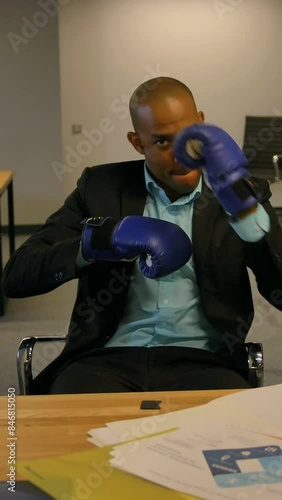 POV. Sporty fighty leader in business concept. Afro-American businessman sitting with boxing gloves in office and makes hand waving and boxes shoots. Slow moton. Vertical shot. photo