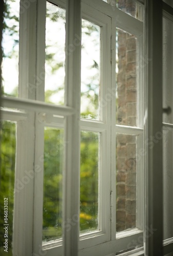 large white window and view of the garden. Green trees outside the window. Vintage apartment interior. White room with a large window