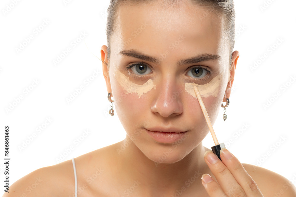 Portrait of a beautiful young woman applying concealer on a white background Portrait of a beautiful young woman applying concealer on a white background