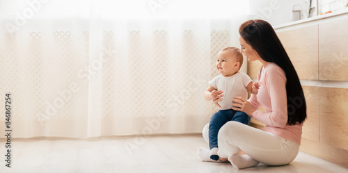 Photography A woman is seated on the floor next to a baby, both engaged in a moment of connection and interaction