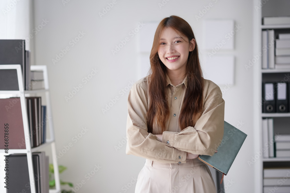 Confident young professional woman in an office setting, smiling and holding a file, showcasing workplace positivity and professionalism. Confident young professional woman in an office setting, smiling and holding a file, showcasing workplace positivity and professionalism.