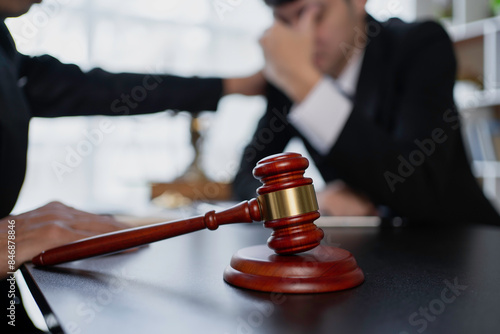 Close-up of a gavel with two people discussing legal matters in a courtroom or office environment, focusing on justice and legal proceedings.