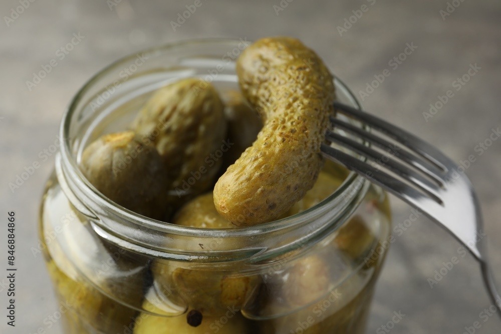 Taking pickled cucumber out of jar on grey background, closeup Taking pickled cucumber out of jar on grey background, closeup