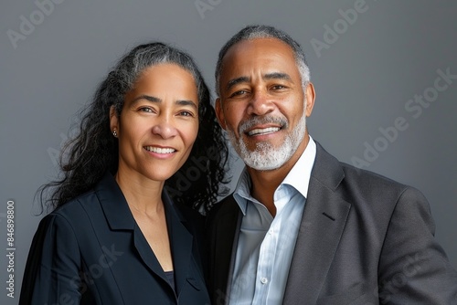 Portrait of a content multiethnic couple in their 50s wearing a professional suit jacket while standing against solid color backdrop