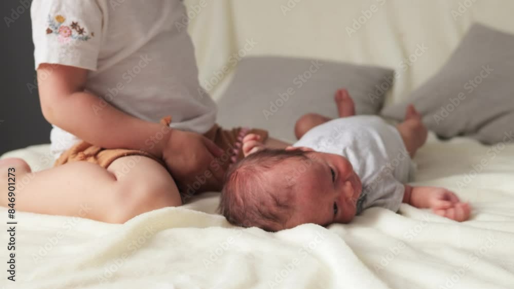 Curly-haired little girl finding joy in spending time with her newborn brother affectionately kissing the infant while playing with him on couch in light home interior Curly-haired little girl finding joy in spending time with her newborn brother affectionately kissing the infant while playing with him on couch in light home interior