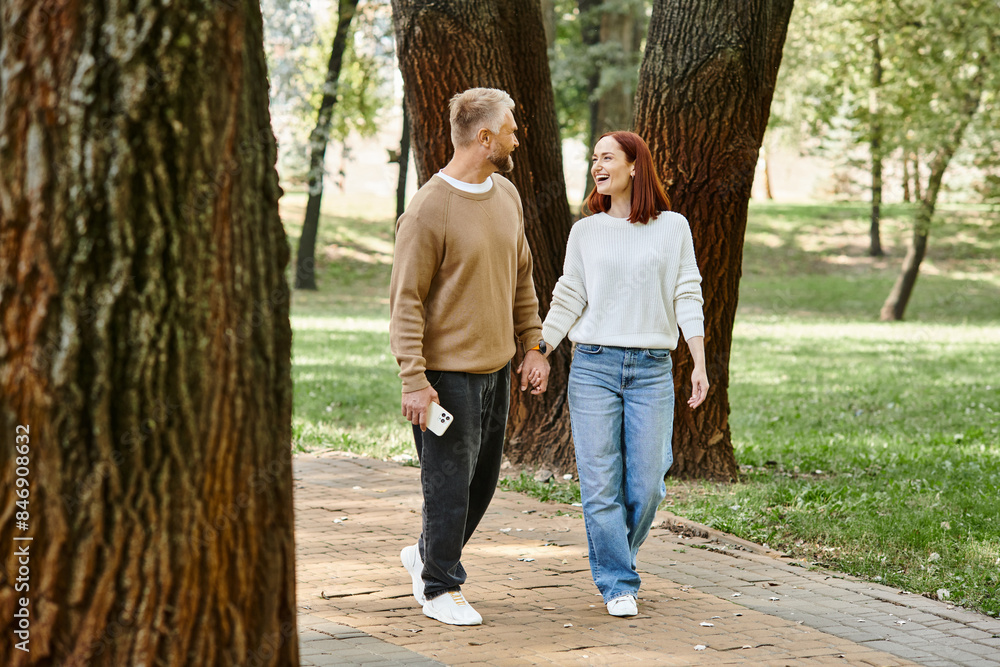 A couple, dressed casually, walk hand in hand in a park. A couple, dressed casually, walk hand in hand in a park.