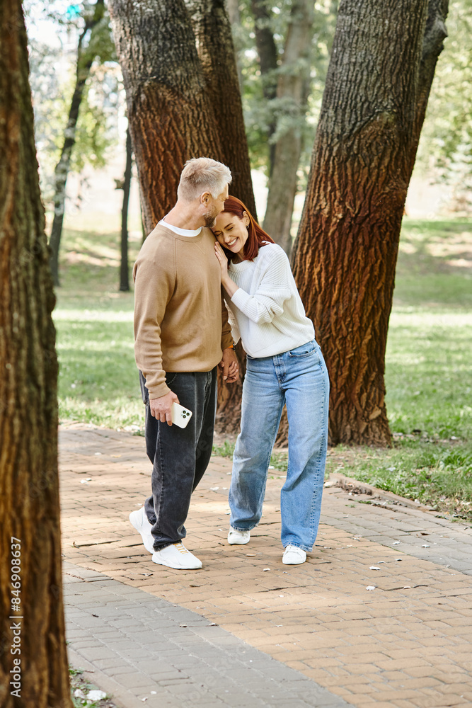 A man and woman in casual attire stand together in a park, surrounded by nature. A man and woman in casual attire stand together in a park, surrounded by nature.