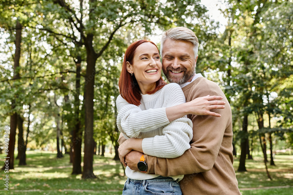 An adult man and woman in casual clothing hug affectionately in a park. An adult man and woman in casual clothing hug affectionately in a park.