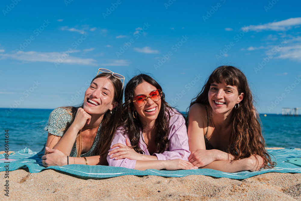 Group of only women lying down on the sand of the beach, smiling and looking at camera. Three young female friends laughing together on the seacoast on a sunny weekend day. Girls enjoying at shore Group of only women lying down on the sand of the beach, smiling and looking at camera. Three young female friends laughing together on the seacoast on a sunny weekend day. Girls enjoying at shore