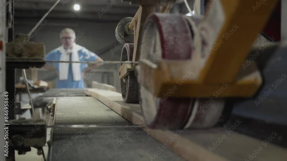 Male Worker Controlling Wooden Board Grinding Process. Board Grinding By Industrial Machine Equipment At A Wood Processing Workshop. Automated Manufacturing Timber Board Grinding Machinery. Male Worker Controlling Wooden Board Grinding Process. Board Grinding By Industrial Machine Equipment At A Wood Processing Workshop. Automated Manufacturing Timber Board Grinding Machinery.