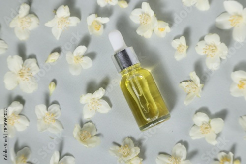 Essential oil in bottle and beautiful jasmine flowers on grey background, flat lay