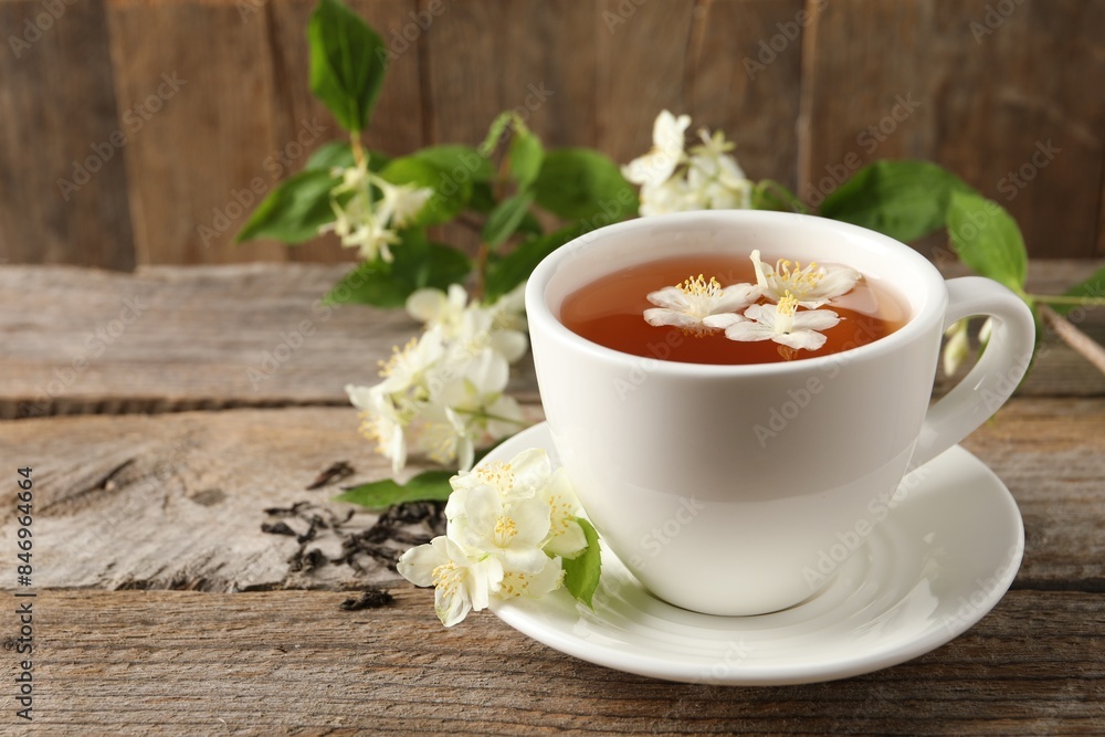 Aromatic jasmine tea in cup, flowers and dry leaves on wooden table, space for text Aromatic jasmine tea in cup, flowers and dry leaves on wooden table, space for text
