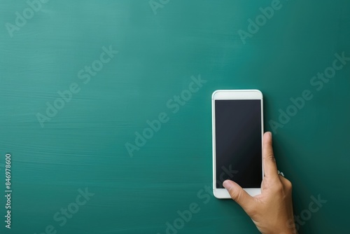 A person holds a smartphone in front of a traditional blackboard, possibly for note-taking or referencing photo