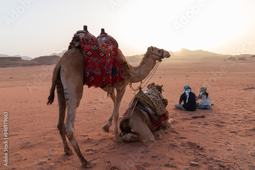 Dos turistas montados en camello durante un paseo al atardecer por el desierto de Wadi Rum, Jordania. photo