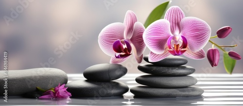 Purple orchid flower placed among three black stones on a shiny reflective surface for a spa zen concept. with copy space image. Place for adding text or design