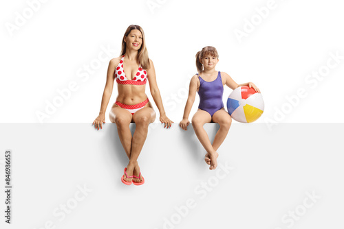 Young woman in bikini and a little girl in a swimming suit sitting on a blank panel