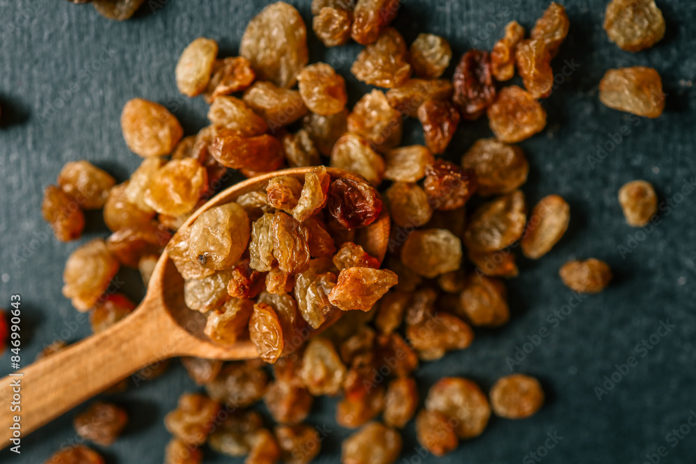 Fototapeta premium Raisins in a wooden spoon scattered on a black background