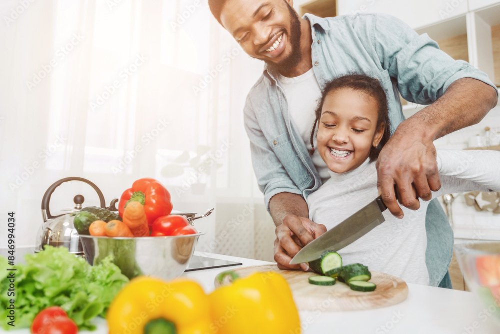 Cheerful Afro Man Showing His Lovely Daughter How To Cut Veggies, kitchen background, free space Cheerful Afro Man Showing His Lovely Daughter How To Cut Veggies, kitchen background, free space