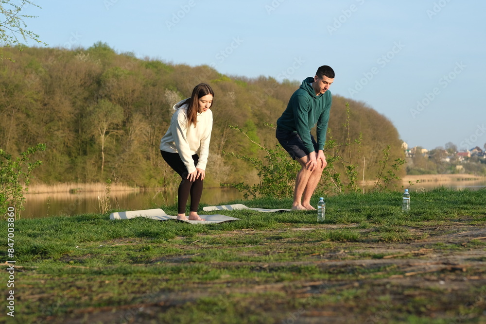 Young couple doing exercises or stretching on the grass, low viewing angle. outdoor sports. Fitness harmony recreation morning seasonal sportive. Young couple doing exercises or stretching on the grass, low viewing angle. outdoor sports. Fitness harmony recreation morning seasonal sportive.