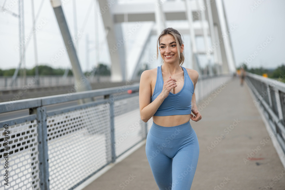 Fototapeta premium Beautiful sporty young woman running over bridge