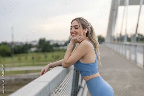 Smiling woman listening music after training on the brigde