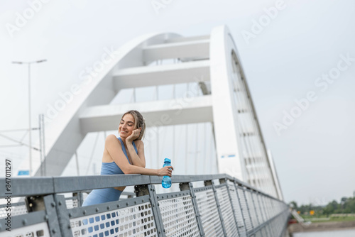 a girl rests after a run and hydrates. he is holding a water bottle and smiling