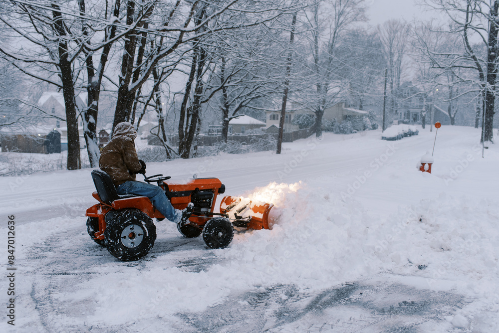 man using old tractor to snow plow his driveway at dusk