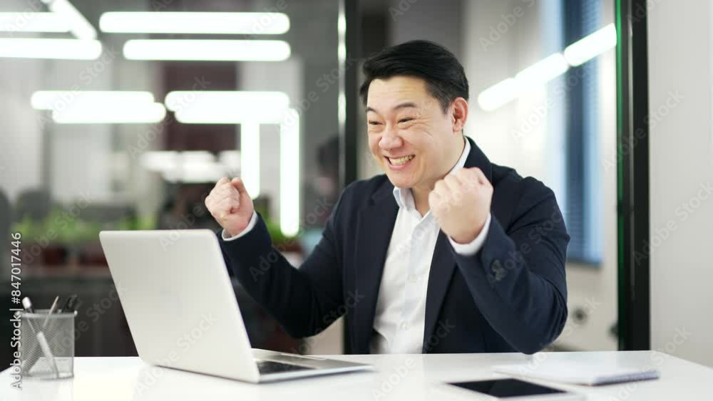 Happy excited asian businessman received great news on laptop while sitting at workplace in business office. Smiling shocked surprised man in a formal suit reads a positive good message on computer Happy excited asian businessman received great news on laptop while sitting at workplace in business office. Smiling shocked surprised man in a formal suit reads a positive good message on computer