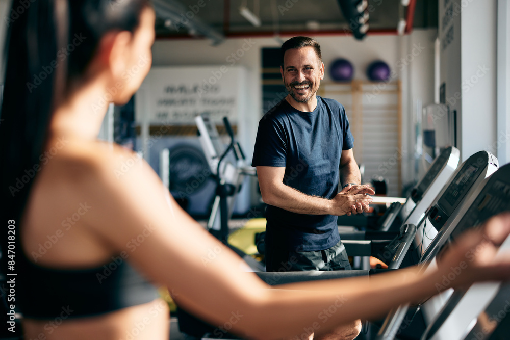 Obraz premium Gym partners, male and female smiling, talking, and walking on a treadmill at the gym.