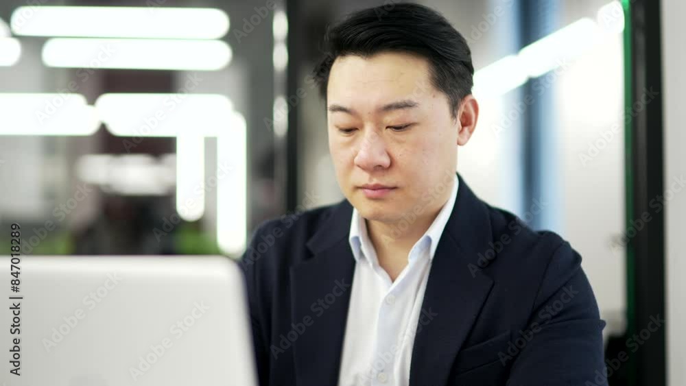 Serious asian businessman is using laptop itting at workplace in business office. Focused man in a formal suit chats online, banking, works in computer app or thinks about a startup project. Close up Serious asian businessman is using laptop itting at workplace in business office. Focused man in a formal suit chats online, banking, works in computer app or thinks about a startup project. Close up