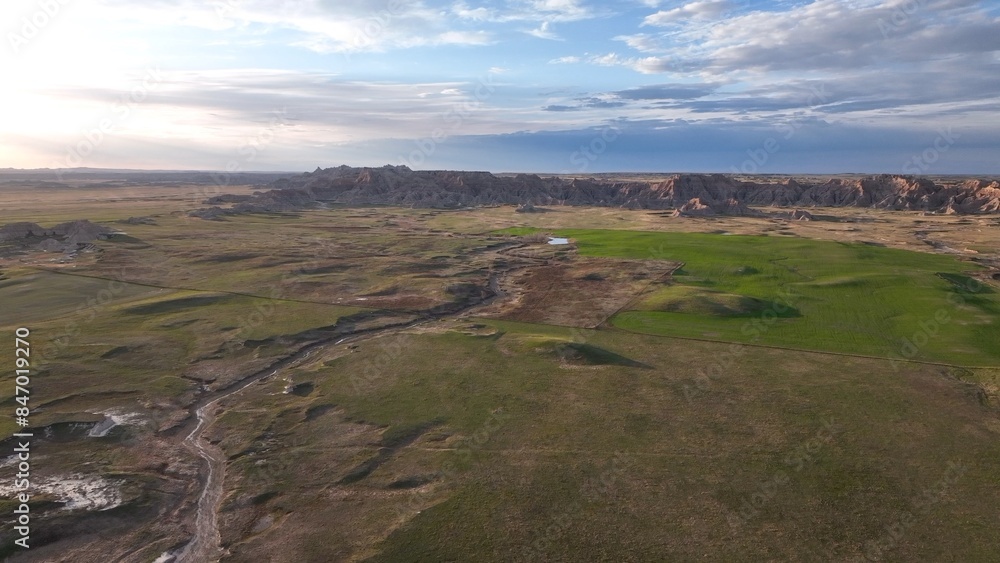 Desert landscape with mixed grass prairie and Badlands National Park in South Dakota mountain range with late afternoon sunshine on ancient geological formations Desert landscape with mixed grass prairie and Badlands National Park in South Dakota mountain range with late afternoon sunshine on ancient geological formations