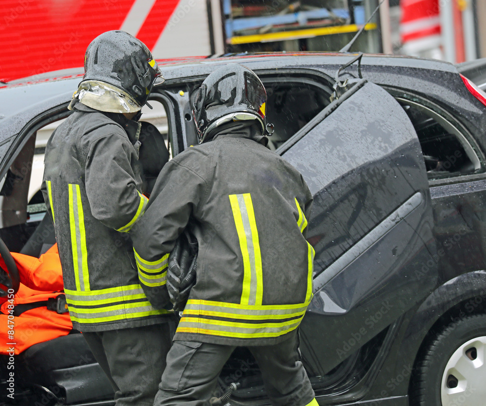Firefighters using jaws of life and ram to pry open door of crashed car on highway Firefighters using jaws of life and ram to pry open door of crashed car on highway