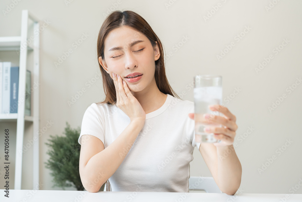 Suffering from toothache, blur asian young woman touch cheek, face expression ache or feel pain, sensitive molar teeth, hand holding glass of water with ice, inflammation when drink cold, healthcare. Suffering from toothache, blur asian young woman touch cheek, face expression ache or feel pain, sensitive molar teeth, hand holding glass of water with ice, inflammation when drink cold, healthcare.