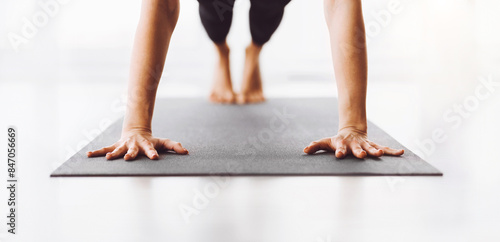 Cropped of woman maintains balance and focus as she performs a yoga pose on a gray mat. Her bare feet and hands are pressed against the surface, suggesting strength and flexibility